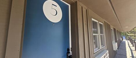 Una puerta azul con el número 5, un teclado de combinación y una ventana con persianas.