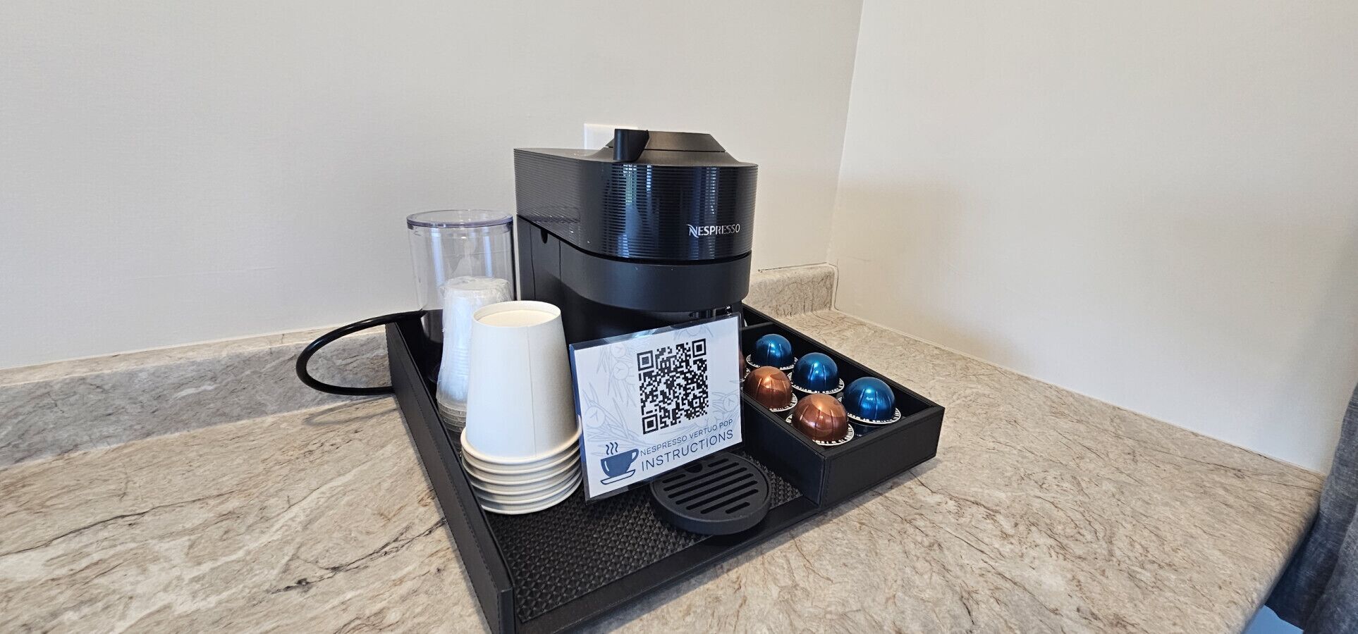 A Nespresso coffee machine, disposable cups, a QR code for instructions, and a tray with chocolate truffles.