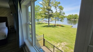 A bedroom with a large window overlooking a grassy area and a body of water. - Juniper Motel-King Suite Deluxe*RM5*Lakefront*ATV Access (Greenville)