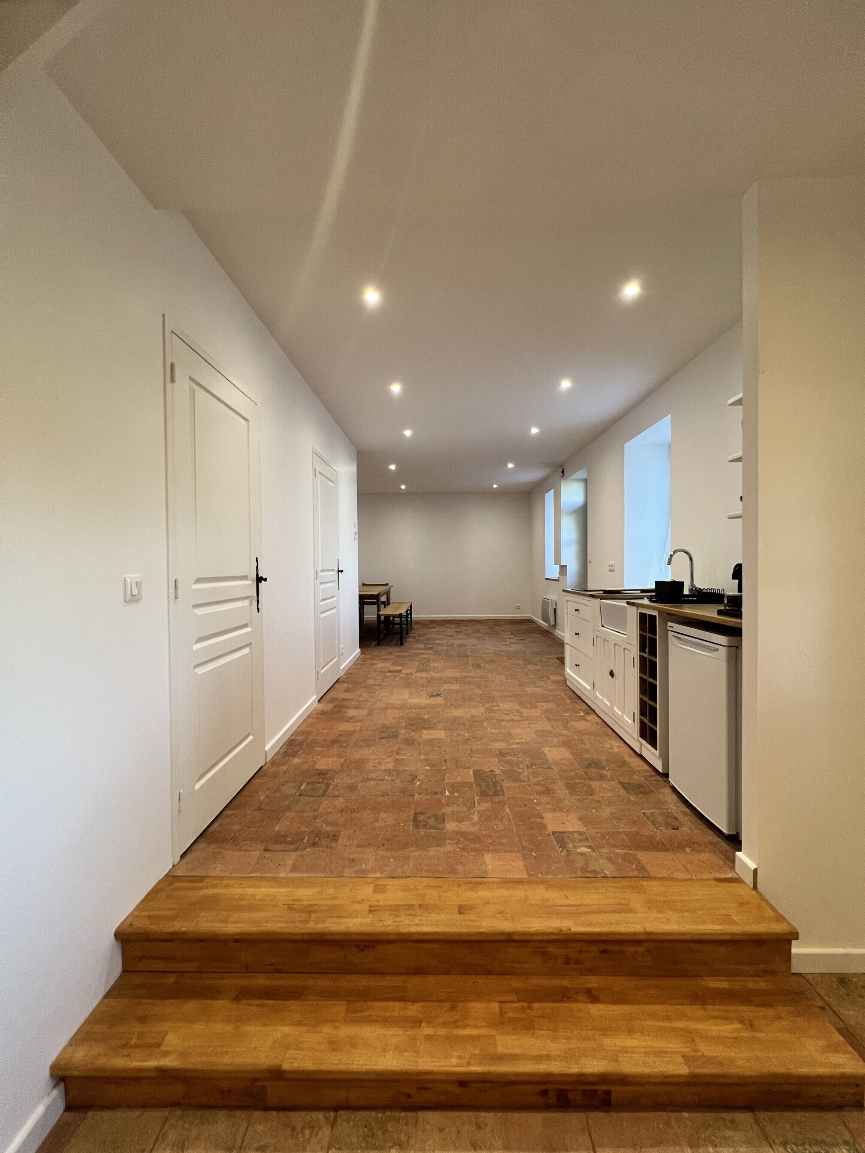 A modern kitchen with white cabinetry, a wooden staircase, and a dining area in the background.