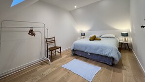 A bedroom with a skylight, a bed with pillows, a chair, and a bedside table with a lamp. - Historic Comfort in the Heart of Ballon (Ballon-Saint-Mars)
