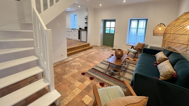 A spacious living area with a staircase, a sofa, a dining table, and a kitchen in the background. - Historic Comfort in the Heart of Ballon (Ballon-Saint-Mars)