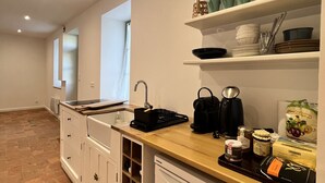 A kitchen with white cabinets, a wooden countertop, and a sink. There are shelves above the countertop holding dishes and a decorative item. - Historic Comfort in the Heart of Ballon (Ballon-Saint-Mars)