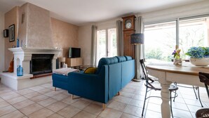 A living room with a fireplace, a sofa, a dining table, and a clock.