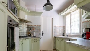A kitchen with light green cabinets, a stove, a sink, and a window with curtains.