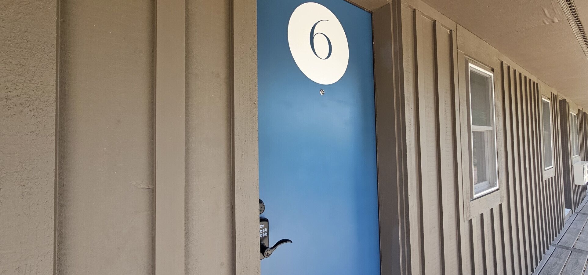 Um edifício com porta azul marcada pelo número 6, um interfone e uma série de janelas ao longo da lateral.