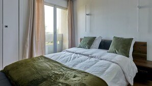 Ein Schlafzimmer mit einem großen Bett, Blick durch eine Schiebetür und einer Holzbank am Fenster.