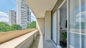 Ein Balkon mit Betonbrüstung, einem Blumentopf und einer Schiebetür.