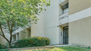 Ein Gebäude mit einer Betonfassade, einem Baum und einem kleinen Gartenbereich mit gelben Blumen und Grünpflanzen.