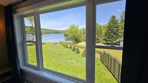 A room with a large window offering a view of a lake, a grassy area, and a forested hill.