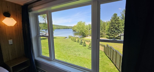 A room with a large window offering a view of a lake, a grassy area, and a forested hill.
