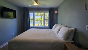 A bedroom with a bed, a ceiling fan, a window with curtains, and a wall-mounted TV.