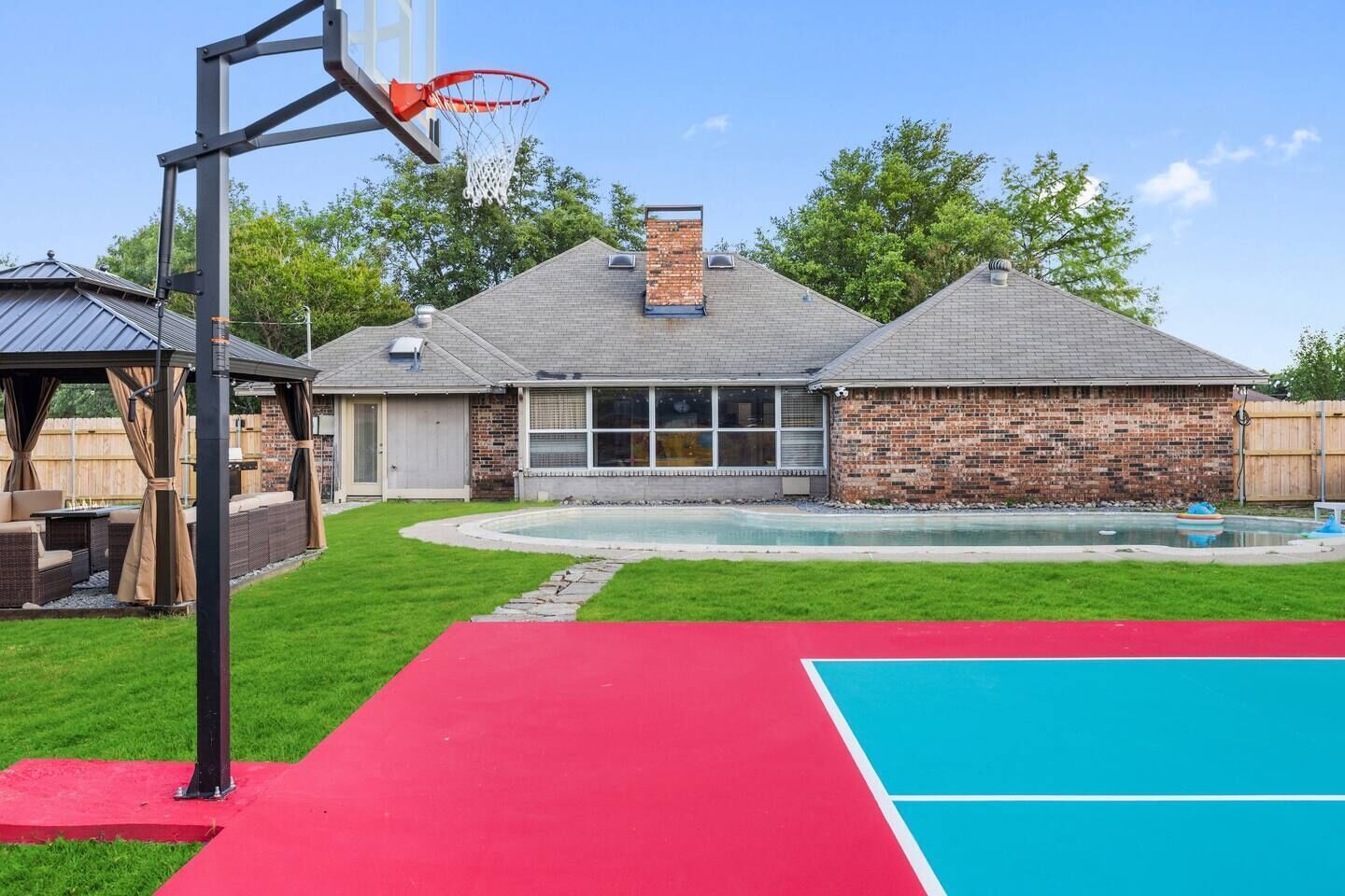 Een achtertuin met een basketbalveld, een zwembad en een overdekt terras.