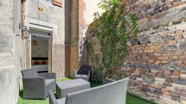 Un cortile con mobili in vimini, un muro in pietra e una recinzione in legno.