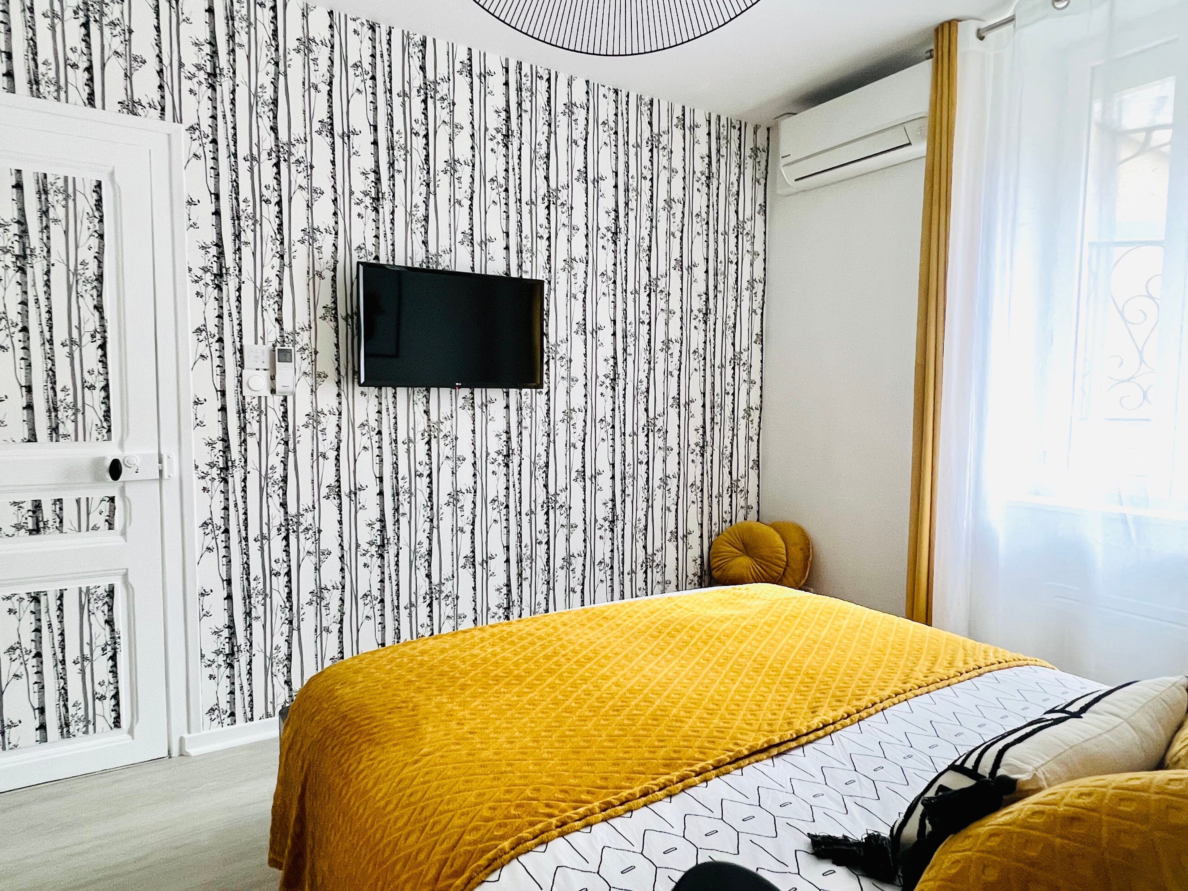 A bedroom with a bed, a television on the wall, and a window with curtains.