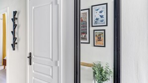 Una porta bianca con maniglia nera, uno specchio con cornice nera e tre opere d'arte appese al muro.