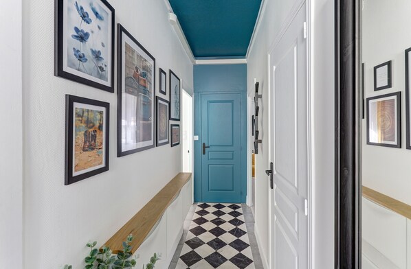 A hallway with a checkered floor, a blue door, and framed artwork on the walls.