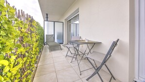 A balcony with a table and chairs, a sliding glass door, and a green climbing plant wall.
