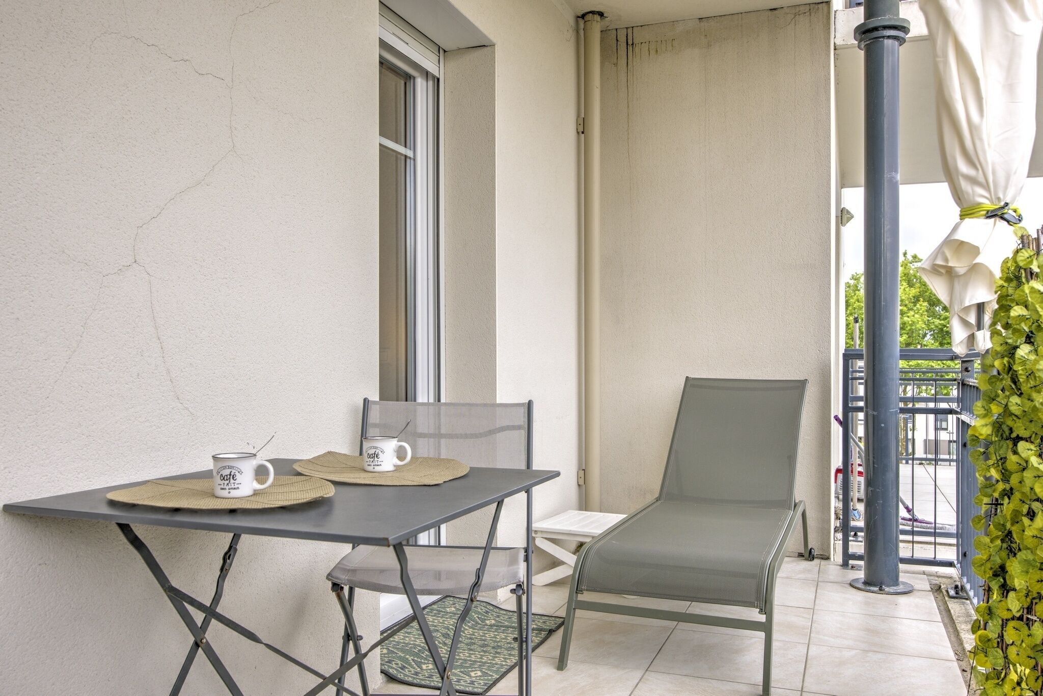 A balcony with a table and chairs, a window, and a view of the street.