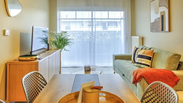 A modern living room with a dining table, sofa, and a large window with curtains.