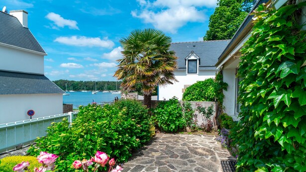 A stone pathway leading to a white house with a view of the sea.