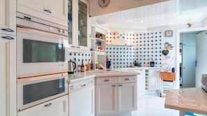 A modern kitchen with white cabinetry, a built-in oven, and a microwave. There is a countertop with various kitchen items and a small wooden table.
