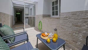 Un patio con una mesa dispuesta para el desayuno, una manguera verde y una ventana.