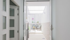 Un pasillo con una puerta de vidrio que da a una habitación con una cama, una mesita con una planta y una silla.