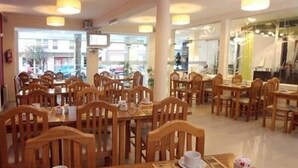 A spacious dining area with wooden tables and chairs, large windows offering a view of the street, and a clean, well-lit interior. - Hotel Patio del Mar (Mar del Plata)
