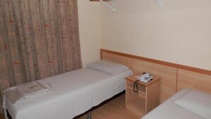 Hotellihuone, jossa on yksi sänky, yöpöytä, jossa on puhelin, ja sängyn yläpuolella oleva puinen hylly.