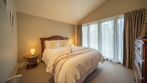 A neatly arranged bedroom with a large bed, a bedside table with a lamp, and a dresser. - Townhouse Retreat - Te Anau Getaway (Te Anau)