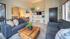 A modern living room with a grey sofa, a wooden coffee table, and a bookshelf filled with books and decorative items. - Townhouse Retreat - Te Anau Getaway (Te Anau)