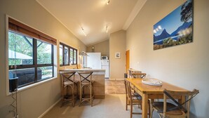 A modern kitchen with large windows, a dining area with wooden furniture, and a mountain landscape painting on the wall. - Townhouse Retreat - Te Anau Getaway (Te Anau)