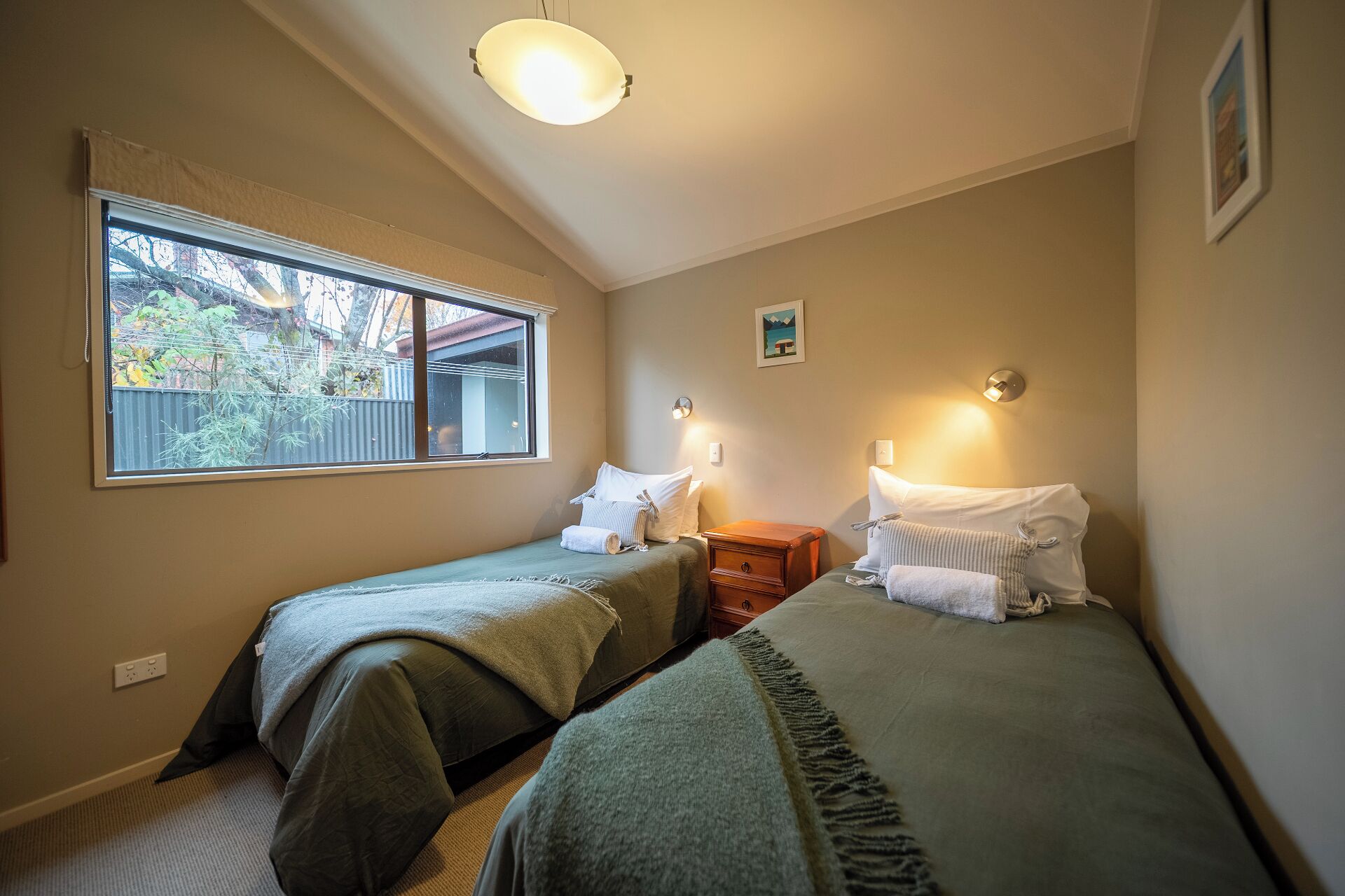 Une chambre avec deux lits simples, une fenêtre donnant sur les arbres et un luminaire au plafond.