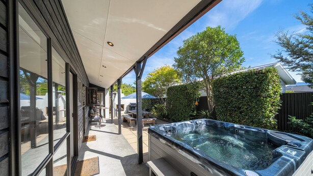 A covered patio area with a hot tub, outdoor seating, and a view of the backyard. - Townhouse Retreat - Te Anau Getaway (Te Anau)