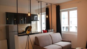 A modern living space with a sofa, a kitchen area, and a large window. - Downtown Living With a View, Ideal for 4 (Le Mans)