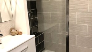 A modern bathroom with a glass shower enclosure, white vanity with drawers, and a tiled backsplash. - Downtown Living With a View, Ideal for 4 (Le Mans)
