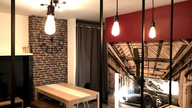 A modern room with a brick wall, a wooden table, and a large window with a car mural. - Downtown Living With a View, Ideal for 4 (Le Mans)