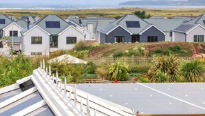 A row of modern houses with solar panels, a grassy field, and a view of the sea. - Sea Sanctuary (Bideford)