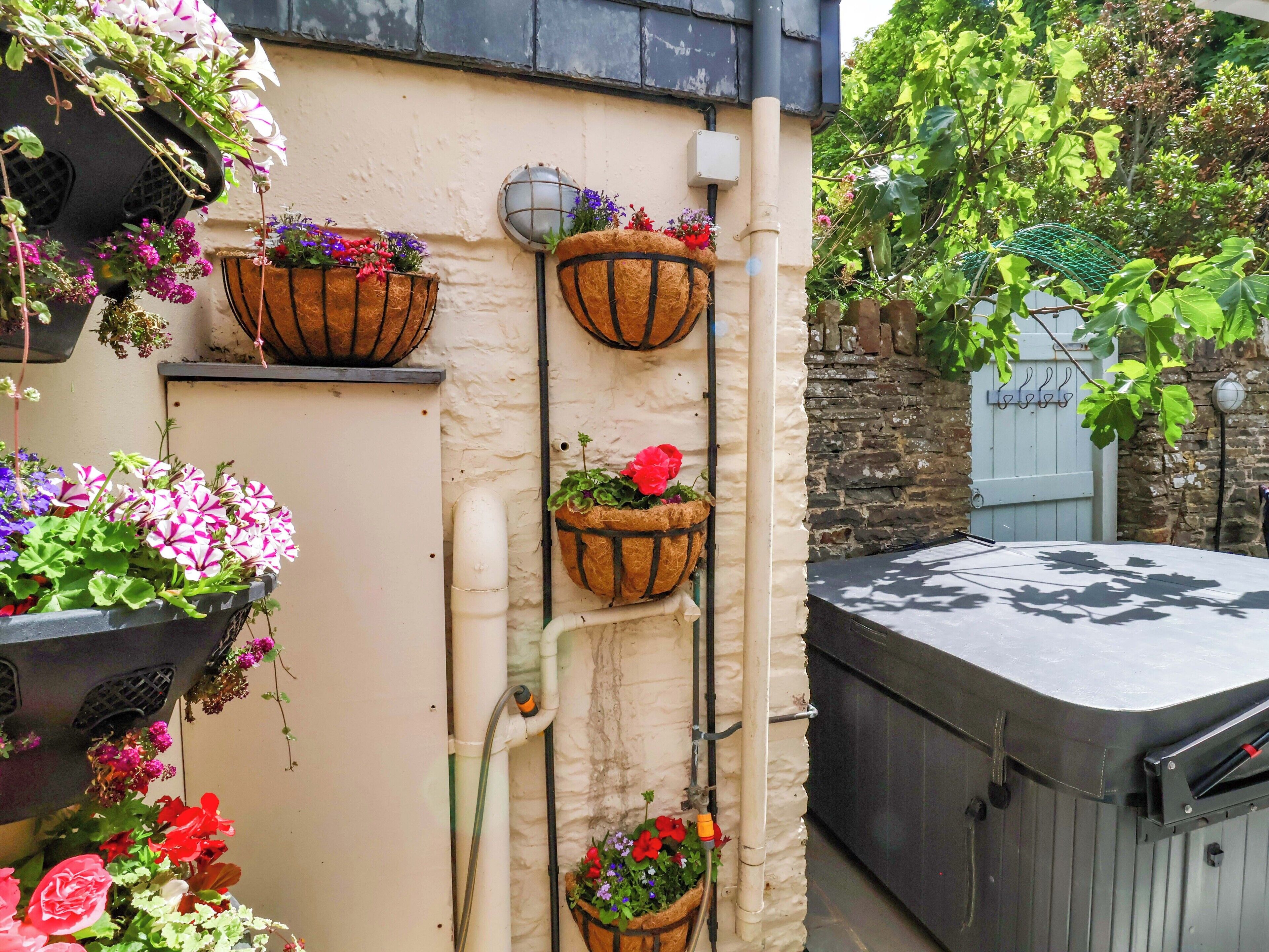 A building with multiple flower planters attached to the exterior wall, a water pipe, and a hot tub area.