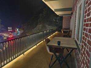 A balcony with a table and chairs, a brick wall, and a view of a road with vehicles. - Hotel Kempty Retreat (Mussoorie)