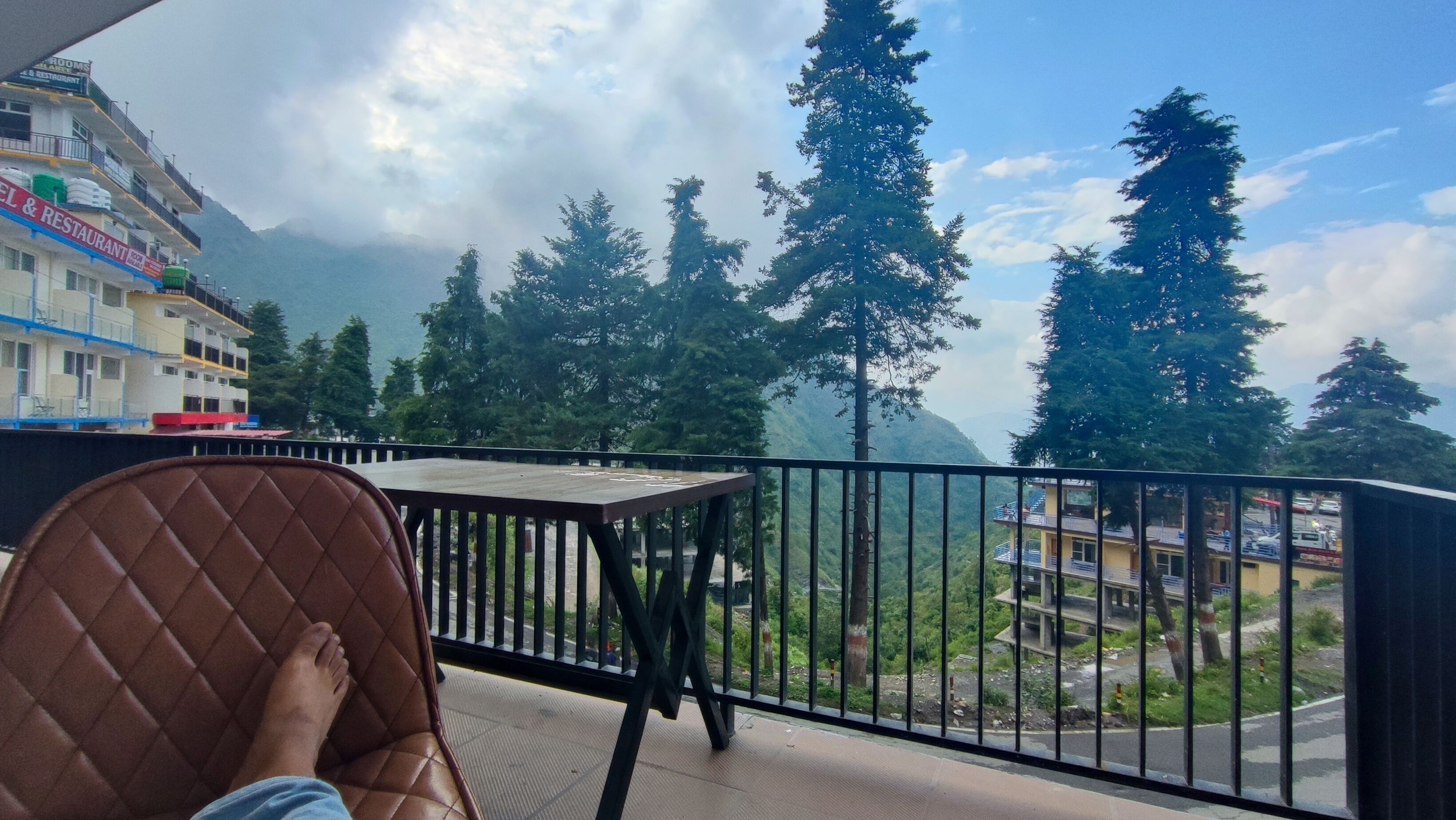 A balcony with a view of a mountain, trees, and a building with a sign for a restaurant.