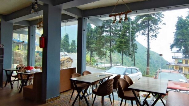Een restaurant met uitzicht op een weg en heuvels, met tafels en stoelen klaar voor een maaltijd.
