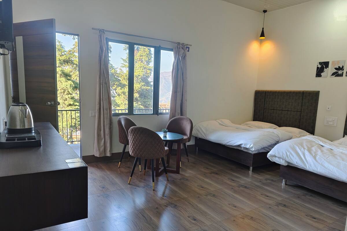 Habitación de hotel con cama, escritorio con hervidor, silla, mesita y balcón con cortinas.