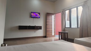 Een hotelkamer met een bed, een aan de muur bevestigde televisie, een raam met gordijnen en een houten deur.