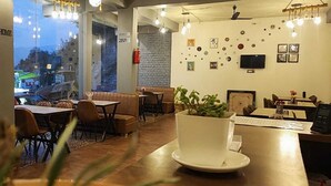 Een gezellig café met houten tafels en stoelen, een grote potplant en een bakstenen muur met decoratieve details.
