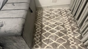 Une pièce avec un canapé gris, un tapis à motifs et un rideau.