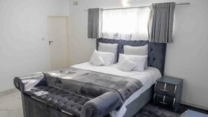 Une chambre moderne avec un grand lit, une tête de lit rembourrée de couleur grise, une literie blanche et un mur d’accent gris.