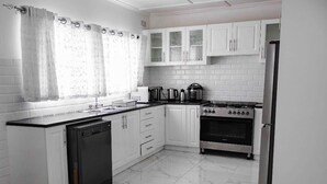 Une cuisine avec des meubles blancs, un lave-vaisselle, une cuisinière et un réfrigérateur.