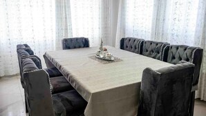 Un espace repas avec une table rectangulaire recouverte d’une nappe de couleur claire, entourée de chaises rembourrées à motifs capitonnés.